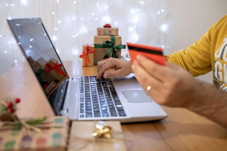 ordinateur ouvert et une femme qui tient une carte bancaire pour effectuer ses achats.Cette photo illustre l'article "Optimiser ses ventes en ligne pour les fêtes 2024"