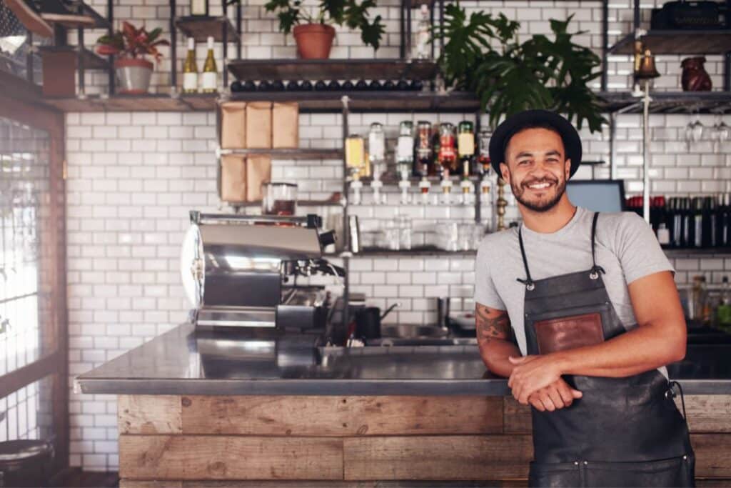 image illustrative de l'article "Référencement Google gratuit" qui represente un homme qui porte un tablier, appuyé sur le comptoir de son café